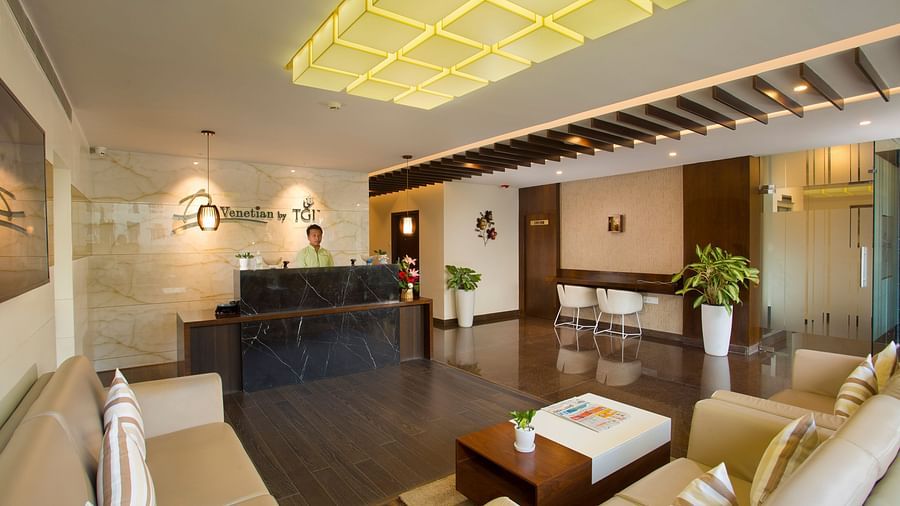 A stylish hotel lobby with beige sofas, a marble reception desk and decorative lighting elements - De Venetian by TGI, Brookefield