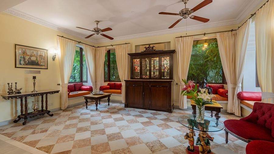 A room with a checkered floor, two ceiling fans, window seating with cushions, and a dark wooden cabinet | Dera Rawatsar, Jaipur