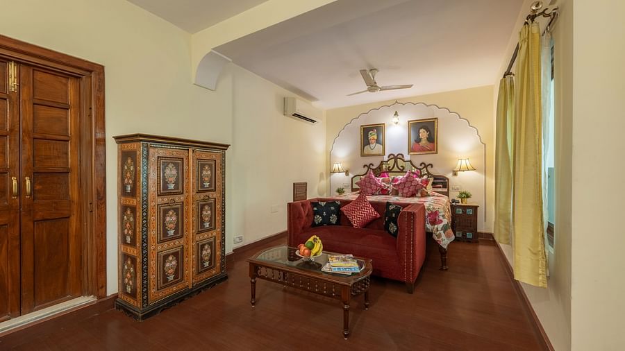 A bedroom with a red sofa, decorative wardrobe, wooden doors, and arched architectural details | Dera Rawatsar, Jaipur