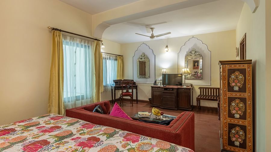 A bedroom with a patterned bedspread, a red sofa, a decorative wardrobe, and arched niches with mirrors | Dera Rawatsar, Jaipur