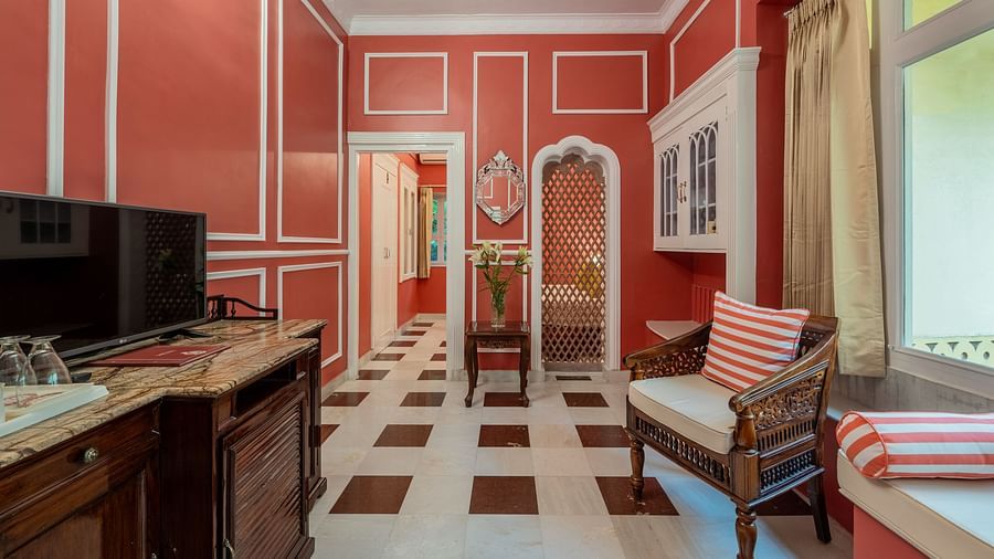 A room with red walls, white trim, a checkered floor, a wooden chair with a striped cushion, and a television | Dera Rawatsar, Jaipur