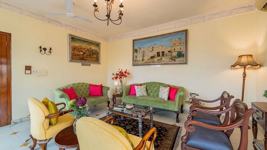 A bright and comfortable living room at Dera Rawatsar, Jaipur, features plush sofas and armchairs, colorful cushions, framed artwork, and a chandelier.