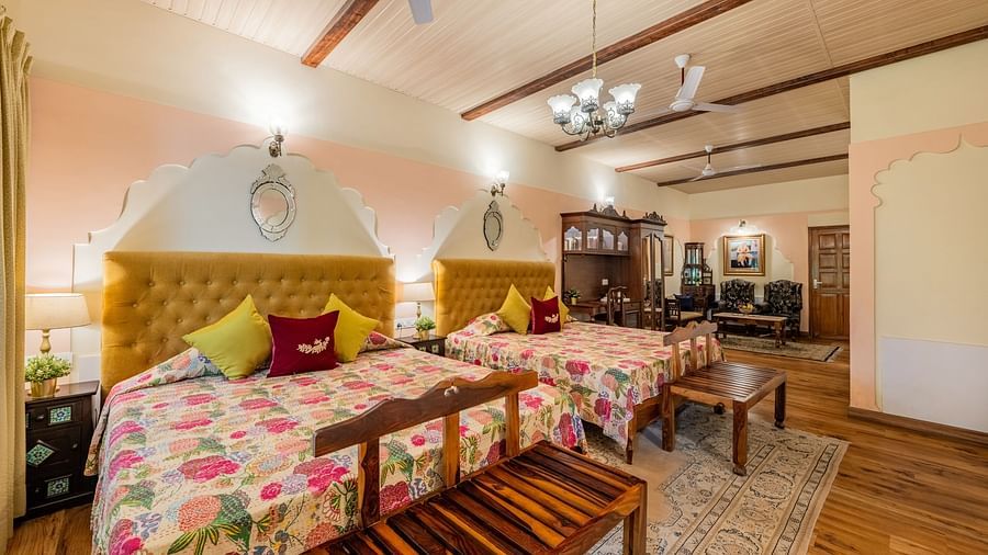 A bedroom with two beds, patterned bedspreads, yellow headboards, a chandelier, and a wooden bench | Dera Rawatsar, Jaipur