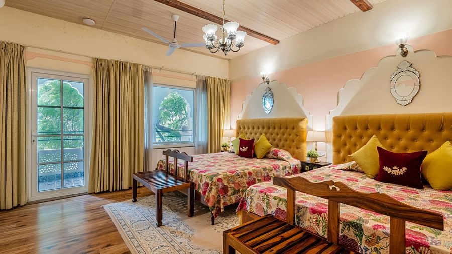 A bedroom with two beds, yellow headboards, a chandelier, wooden beams, and French doors to a garden | Dera Rawatsar, Jaipur