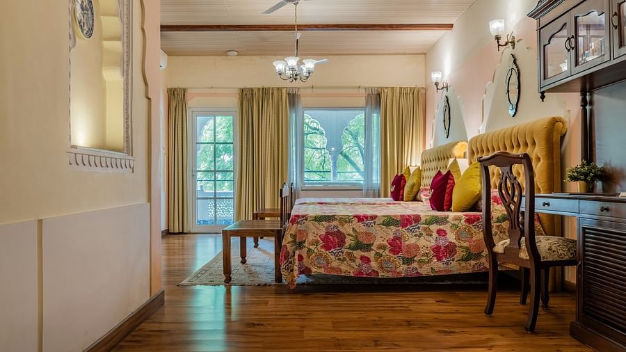A bedroom with two beds, yellow headboards, wooden floors, French doors, and a decorative wall mirror | Dera Rawatsar, Jaipur