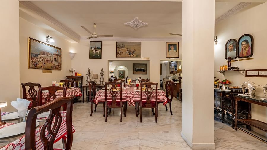 The inviting dining space at Dera Rawatsar, Jaipur, features multiple set tables with patterned cloths, wooden chairs, and an array of framed pictures on the walls.
