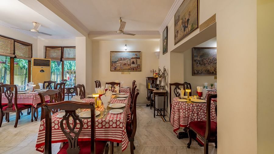 A long, narrow dining room with set tables, wooden chairs, artwork on the walls, and ceiling fans | Dera Rawatsar, Jaipur