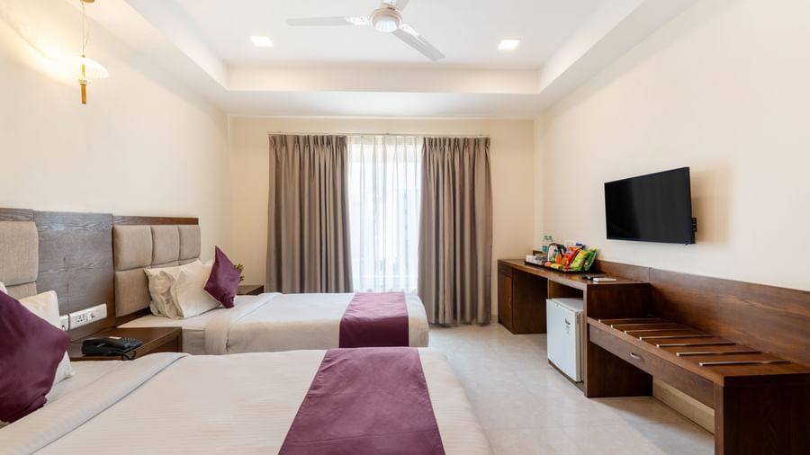 A Deluxe Room at Destino by Monday Hotels, Gachibowli, with twin beds, a work desk, a wall-mounted TV, and a large window.