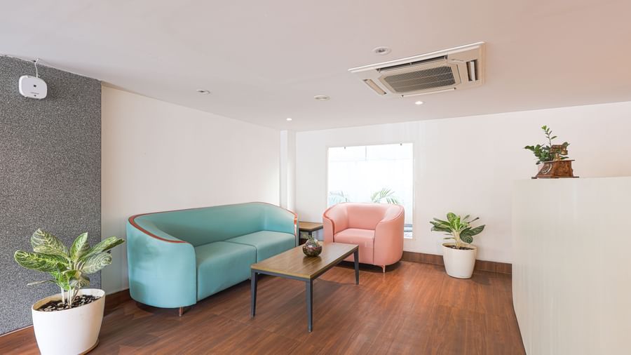 A modern and clean lobby area at Destino by Monday Hotels, Gachibowli, with a blue sofa and a pink armchair.