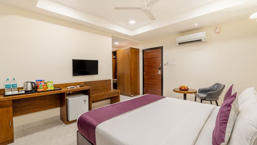 A well-lit room at Destino by Monday Hotels, Gachibowli, featuring a neatly made double bed, a wall-mounted TV, and wooden furnishings.