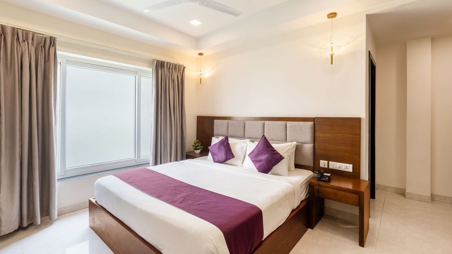 A Premium Room at Destino by Monday Hotels, Gachibowli, with a large double bed with purple accents and a ceiling fan, illuminated by natural light from a large window.