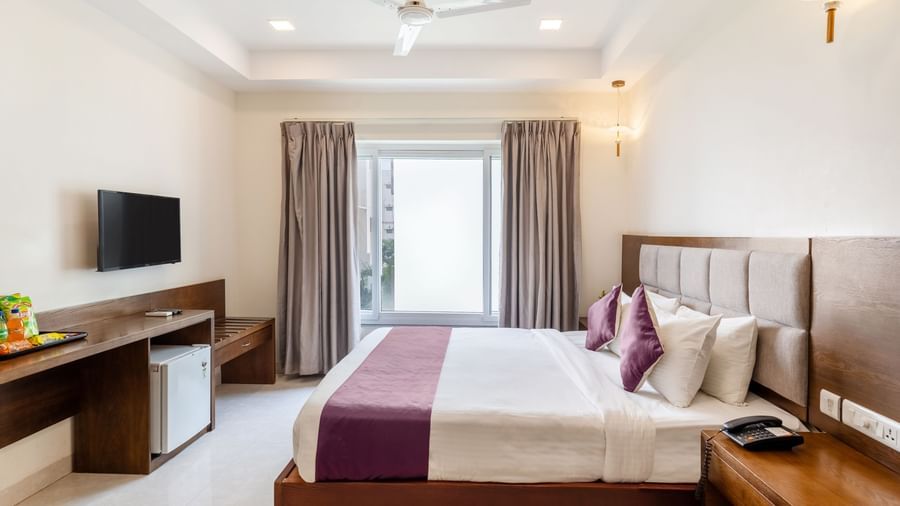 A well-lit room at Destino by Monday Hotels, Gachibowli, featuring a neatly made bed with a purple runner, a wooden desk with a minibar, and a large window.