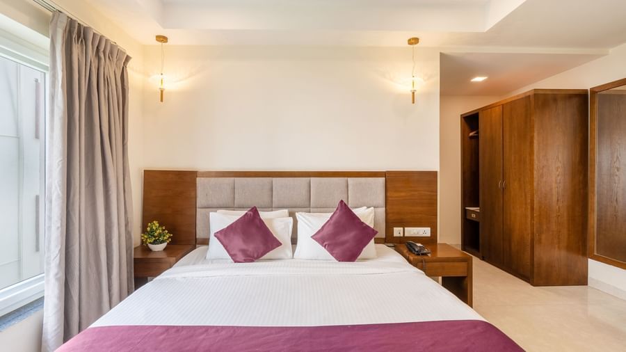 A well-lit room at Destino by Monday Hotels, Gachibowli, featuring a neatly made double bed with purple accents and a spacious wooden wardrobe.