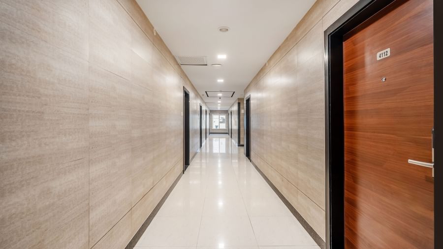 A clean and well-lit hotel corridor at Destino by Monday Hotels, Gachibowli, with a polished tile floor and multiple wooden doors leading to the rooms.