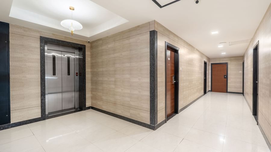 A modern and clean corridor at Destino by Monday Hotels, Gachibowli, with an elevator and wooden doors leading to the rooms.