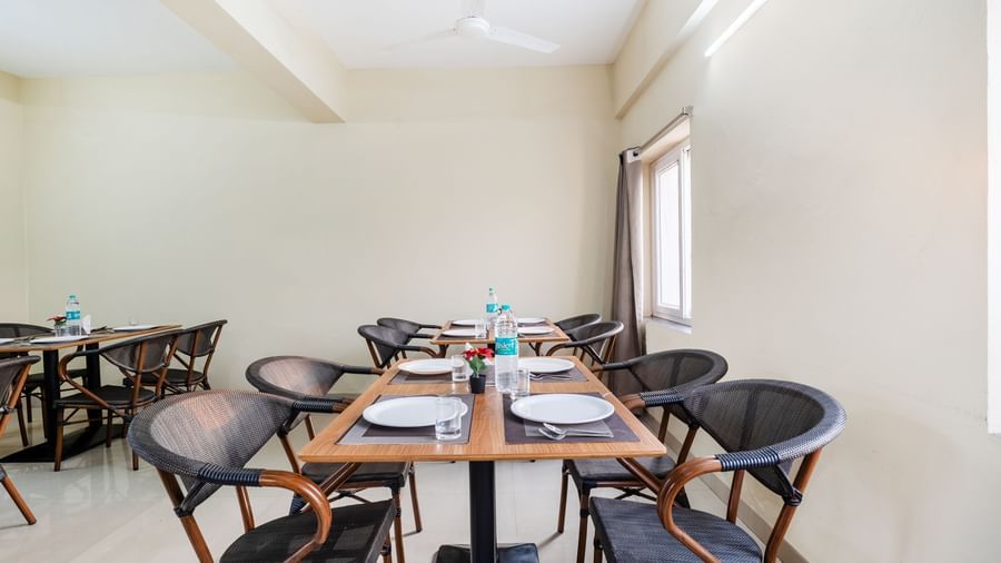 An empty dining area at Destino by Monday Hotels, Gachibowli, with 2 dining tables and woven chairs, set up with plates and water bottles.