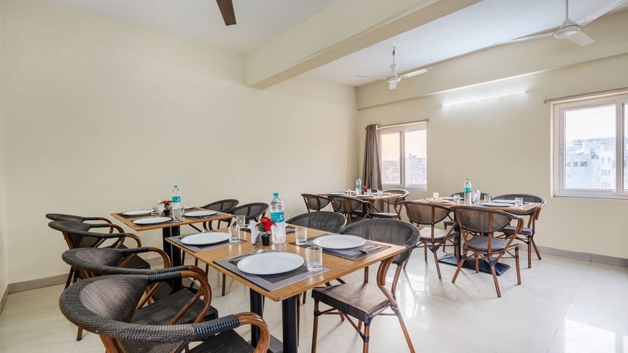 A dining area at Destino by Monday Hotels, Gachibowli, with 2 dining tables and woven chairs, set up with plates and water bottles.
