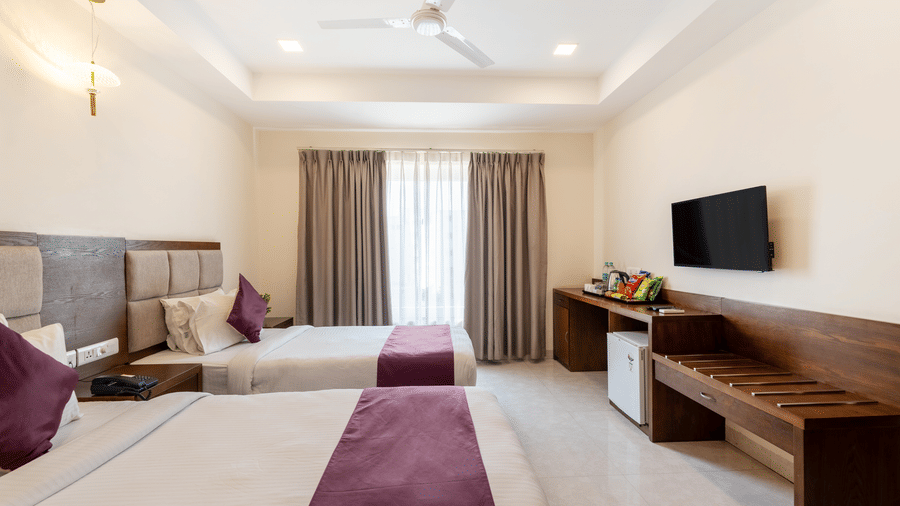 A Superior Twin Room at Destino by Monday Hotels, Gachibowli, with twin beds, a work desk, a wall-mounted TV, and a large window.