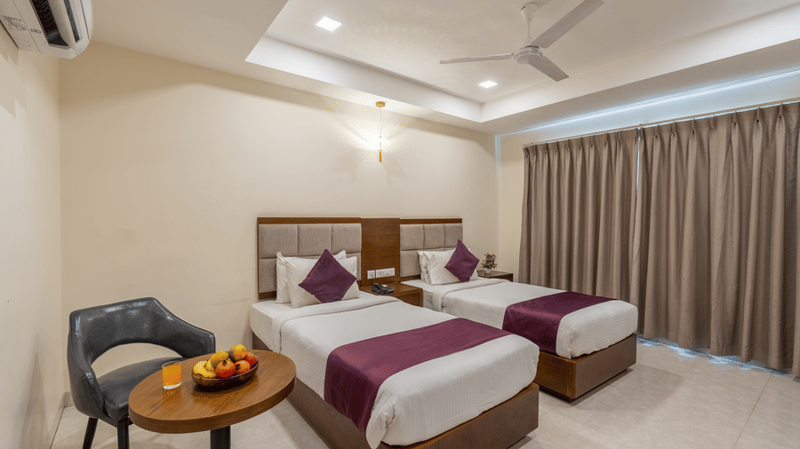 A Superior Twin Room at Destino by Monday Hotels, Gachibowli, with twin beds, a small table with a fruit basket, and a window with its drapes closed.