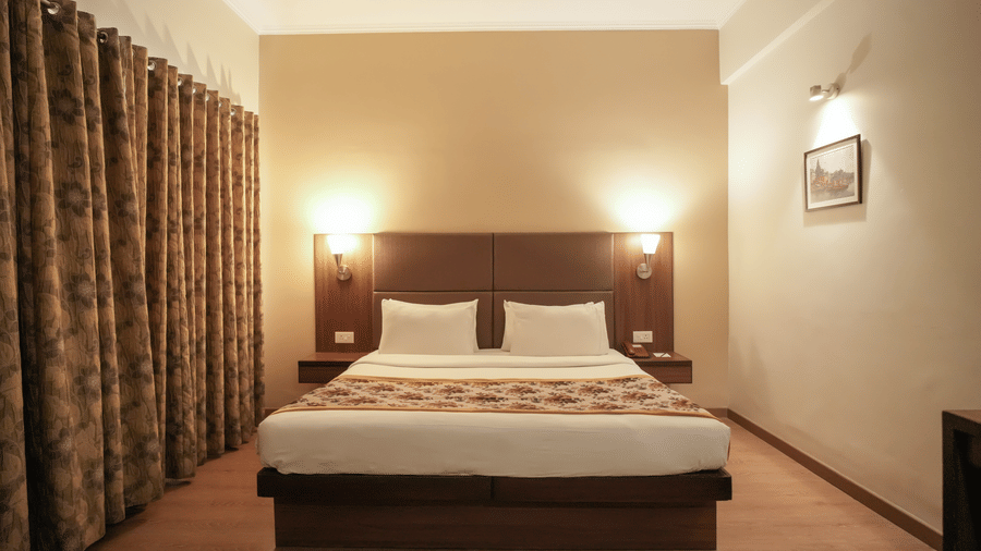 A bedroom at Diamond Hotel Varanasi features a dark wood headboard, warm lighting, and patterned curtains.