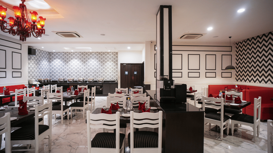 The restaurant at Diamond Hotel Varanasi features white furniture, red accents, and a distinctive red chandelier.