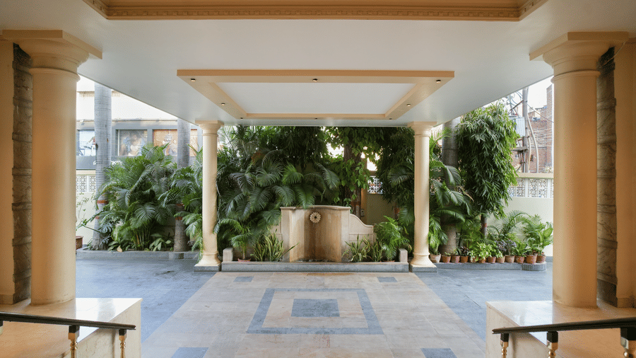 The covered entrance at Diamond Hotel Varanasi features a tiled floor, stone pillars, and lush tropical plants.