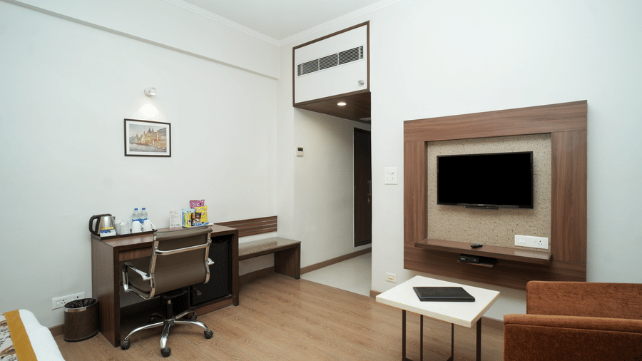 The minimalist interior of a Diamond Hotel Varanasi room offers a television, seating, and a dedicated vanity area.