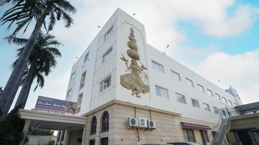The multi-storey facade of Diamond Hotel Varanasi features a decorative mural and tall palm trees against the sky.