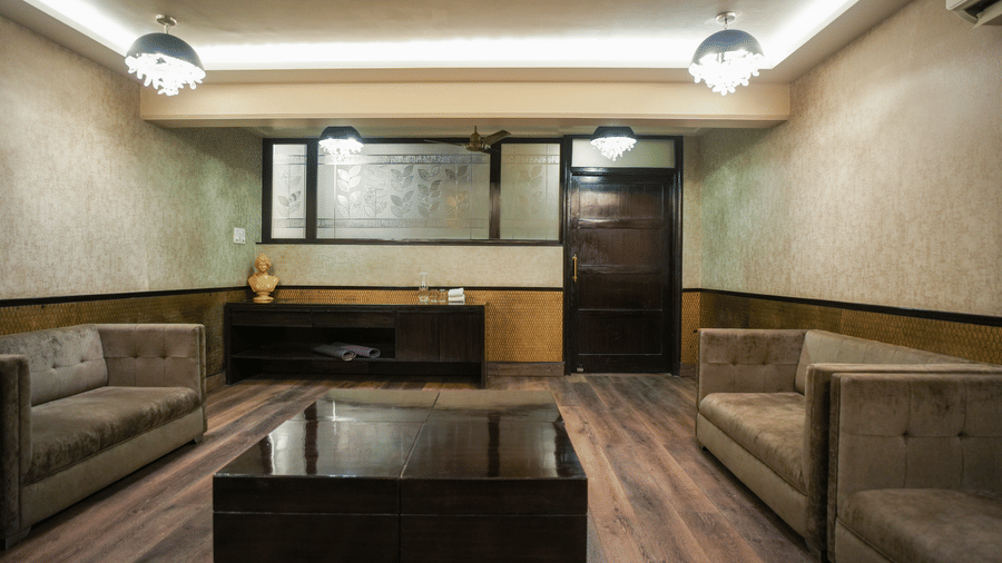 A hall at Diamond Hotel Varanasi features grey sofas, a dark coffee table, and wood-style flooring.