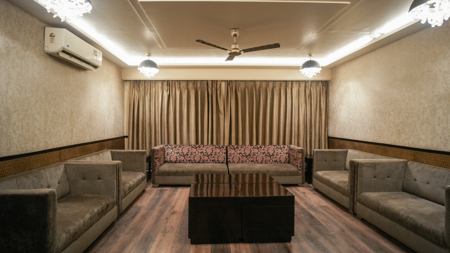 Plush seating is arranged around a central table in a cosy, air-conditioned lounge at Diamond Hotel Varanasi.