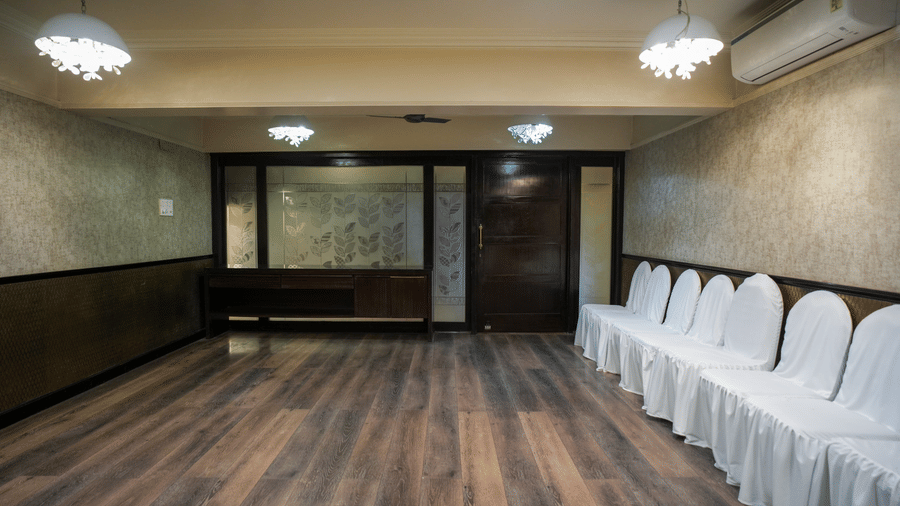 A minimalist meeting room at Diamond Hotel Varanasi displays a polished wood floor and a row of white chairs.
