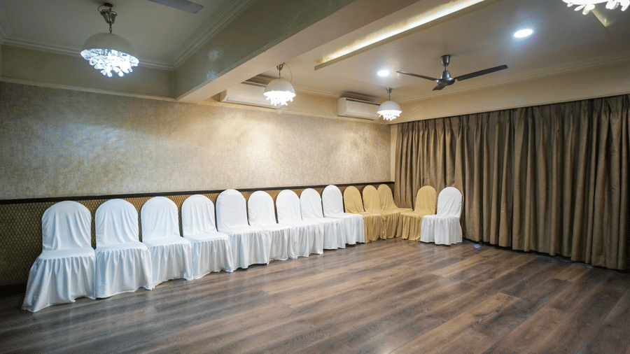 A row of white-clad chairs stands against the wall in a wood-floored hall at Diamond Hotel Varanasi.