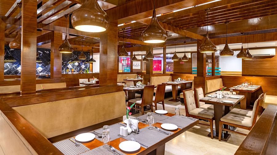 Warmly lit restaurant at Diamond Palace Lords Plaza with wooden beams, set tables, and booth seating.