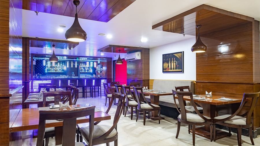 Modern restaurant at Diamond Palace Lords Plaza with wooden tables, chairs, pendant lights, and a bar area.