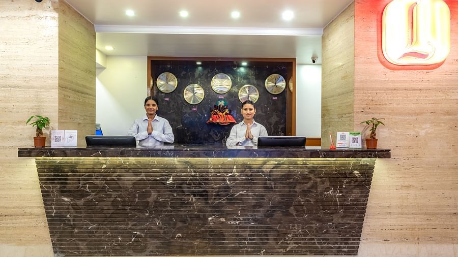 Hotel reception at Diamond Palace Lords Plaza with two staff members behind a marble counter and world clocks on the wall.