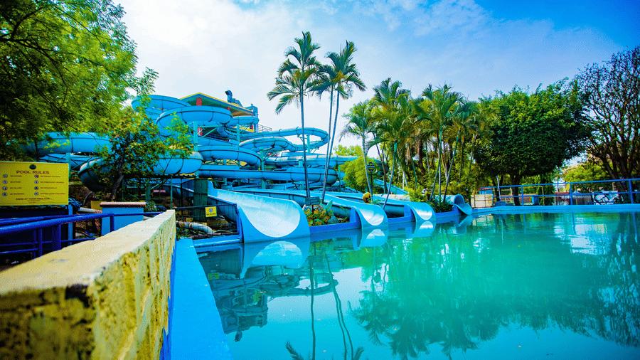 Luxurious water park with multiple slides and pools surrounded by palm trees, clear blue sky | Diamond Parks, Pune