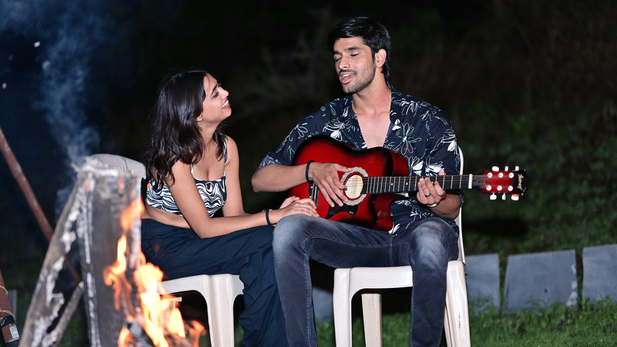 A woman listening to a man playing guitar by a campfire at the adventure camp in Pune at Diamond Parks, Pune.