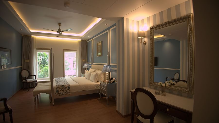 A room with Dileep Kothi, Jaipur with a double bed a dressing table and pastel blue and white striped walls