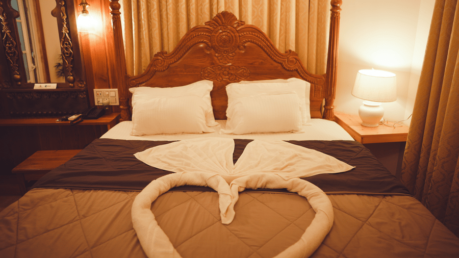Front view of the king size bed with 2 pillows kept at the far end of the room with a table lamp kept on the side table | Dip Holidays