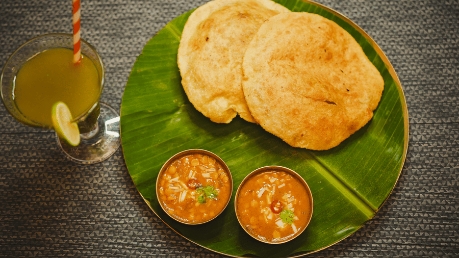 Two deep fried bread and lentil soup served on a banana leaf plate along with a refreshing beverage .