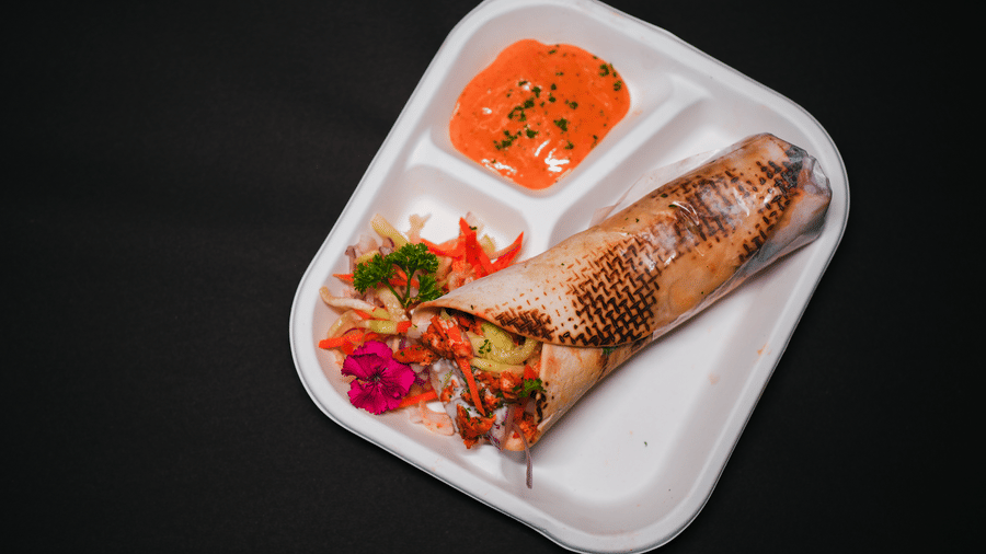 A grilled wrap with fresh salad and dipping sauce, beautifully plated on a white tray at D Café in Dip Holidays.