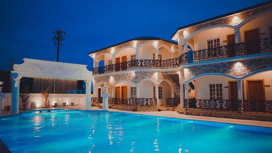 facade image of dip holidays hotel in birbhum with exterior lights switched on with an expansive blue swimming pool in the foreground