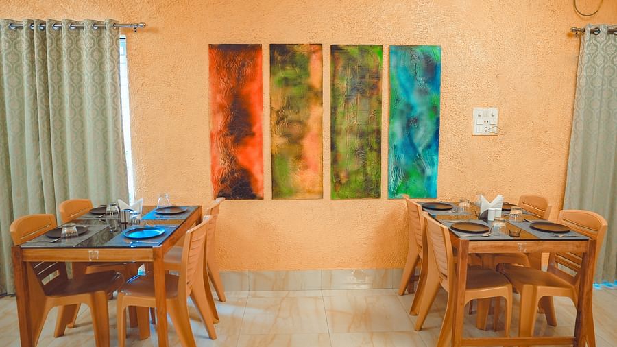 image featuring a series of wall mounted painitngs with dining tables on either side of it at mache vate banagali - Dip Holidays, Birbhum