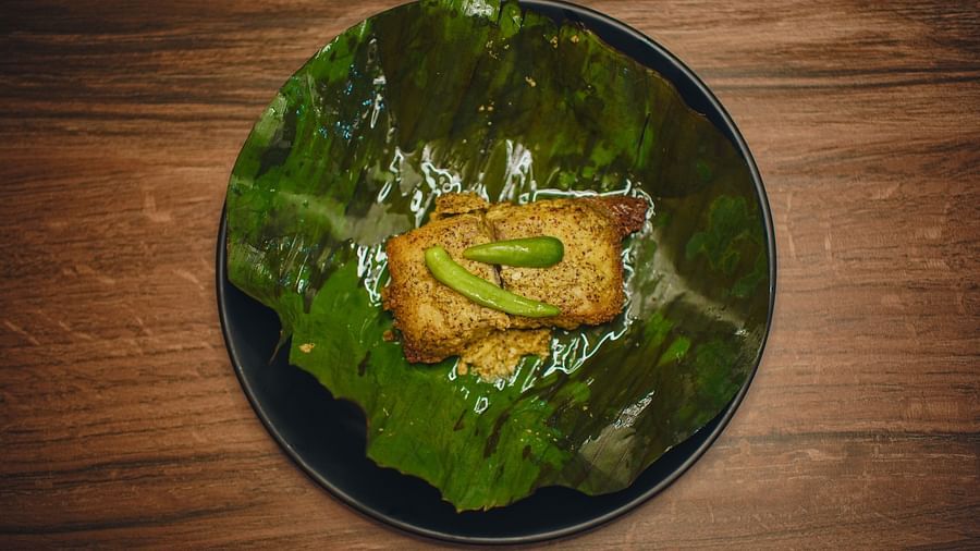 image of a fish preparation made with mustard steamed inside a banana leaf topped with two green chillies - Dip Holidays, Birbhum