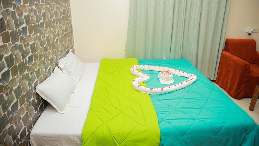 side view of the king size bed with a teal and green coloured comforter spread over it with pastel coloured curtains in the far end of the room