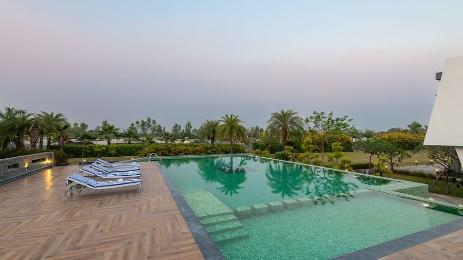 Swimming pool at DLS Forest Vines Resort, surrounded by lounge chairs and offering a tranquil view of trees.