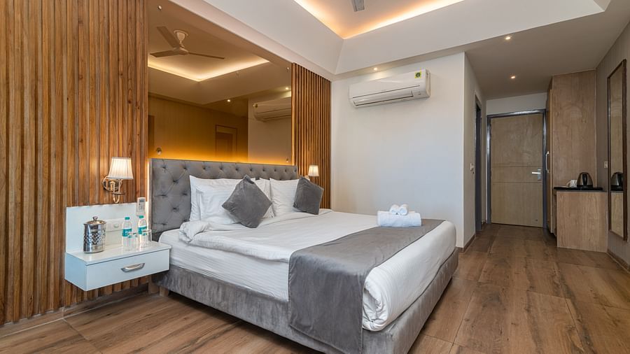 An image of a deluxe room featuring a mirror on the accent wall behind the bed also featuring bed side tables, lamps and other room amenities - DLS Ganga Bliss, Haridwar