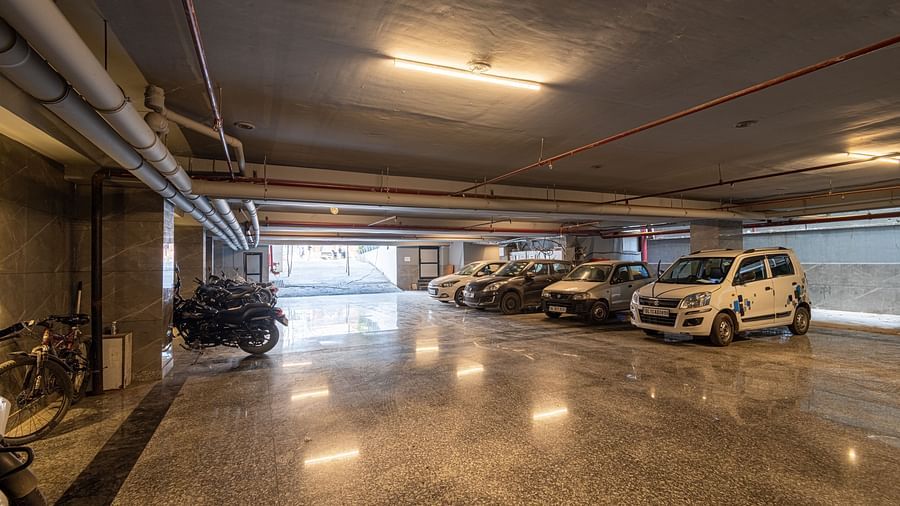 Image of a large parking space at DLS Grand Luxotica, Dehradun featuring cars and bikes parked in warm lighting