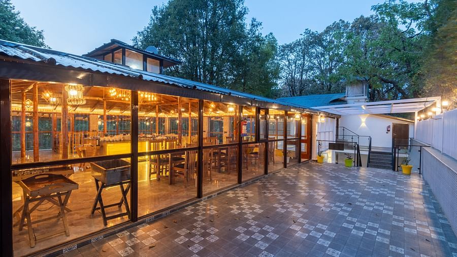 A shot of the restaurant taken from outside featuring the outdoor seating area and trees in the background - DLS The Emerald, Nainital
