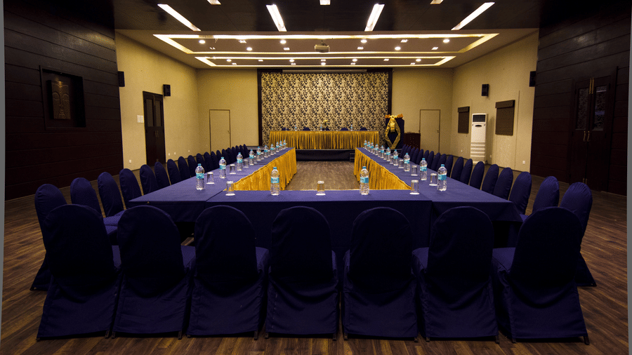 A formal meeting room at DNC Shevaroys Resort & Spa with a U-shaped table covered in fabric and surrounded by chairs.